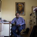 Sokhaya Nkosi sits in his office with a portrait of Es’kia Mphahlele by artist Mbongeni Richman Buthelezi, behind him, Photo courtesy of Oupa Nkosi.
